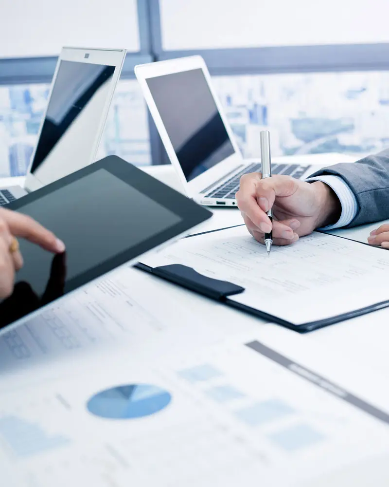 Hands reviewing financial charts with tablet and laptops